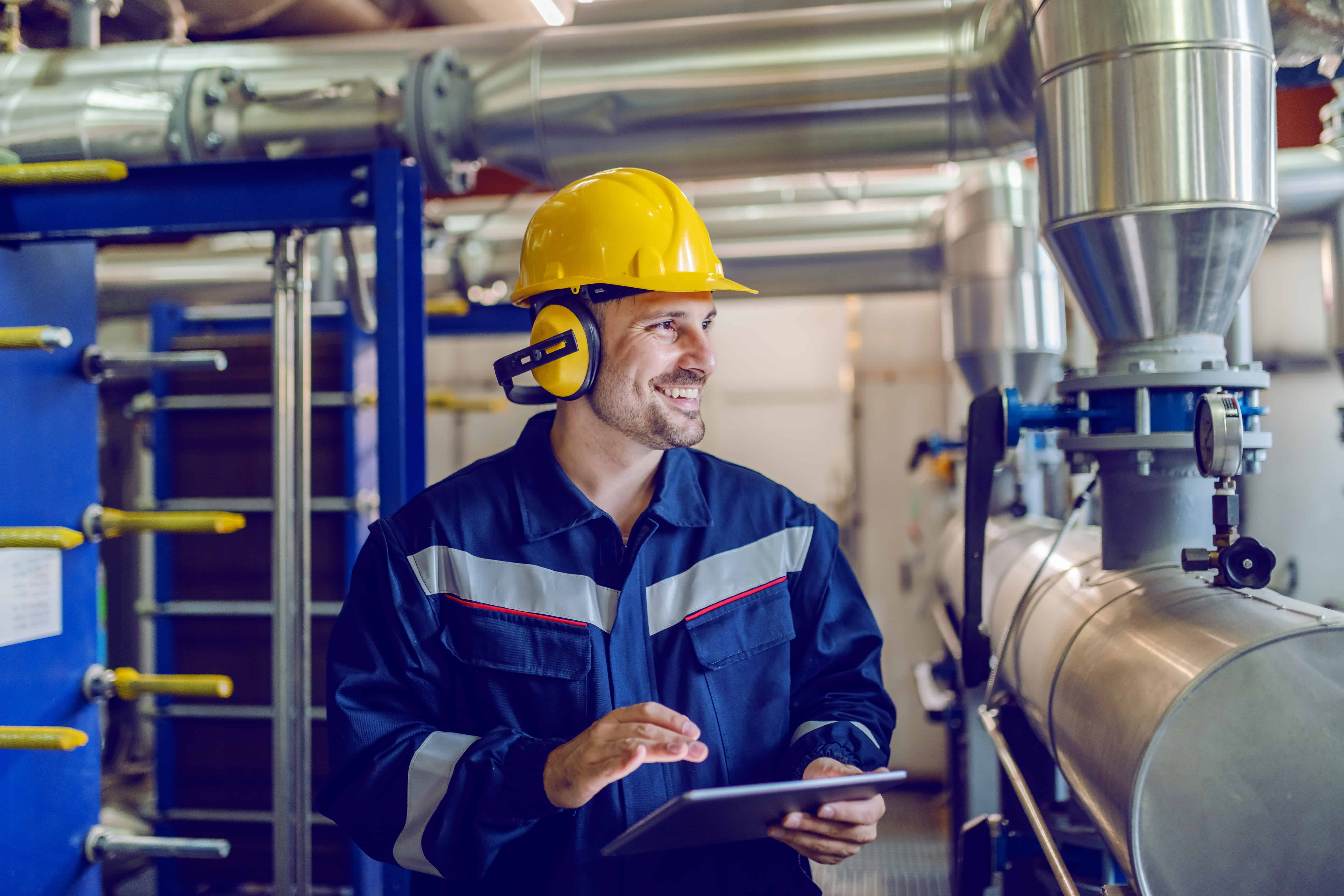 Dedicated smiling factory worker standing next to boiler and hol Dedicated smiling factory worker